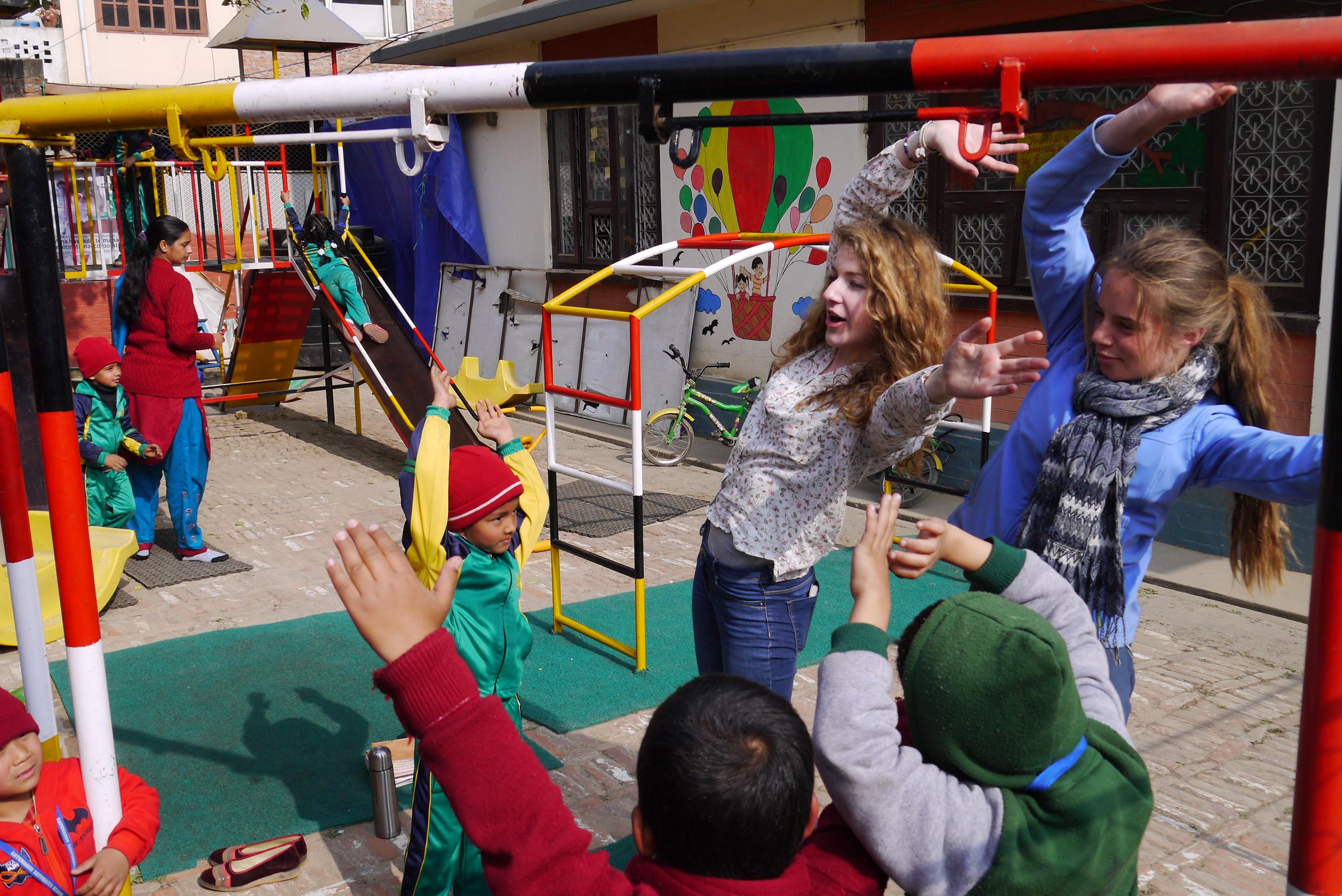 Volunteers between on a group trip play a game with children on the playground as part of their childcare work in Nepal. As part of community work in Nepal, Projects Abroad volunteers on a group trip lead an activity on the playground.